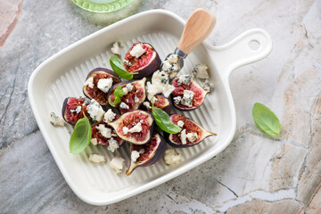 Beige serving tray with fresh torn figs and blue cheese, horizontal shot on a light-grey granite background, high angle view
