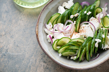 Close-up of salad with fresh cucumber slices, feta cheese and red onion, horizontal shot on a beige granite background, selective focus