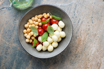 Bowl with scamorza, smoked perlini, cherry tomatoes and basil, flat lay on a beige and grey granite background