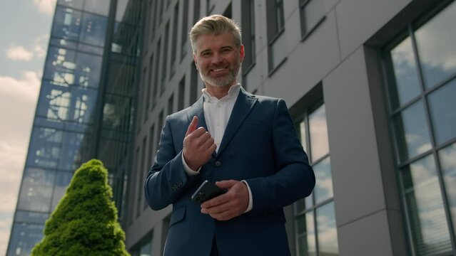 Friendly Caucasian businessman in city with smartphone invite come here gesture old senior mature business employer retired man with mobile phone showing welcome inviting interview join to job company
