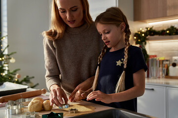 Fototapeta premium Caucasian mother and daughter making gingerbreads in domestic kitchen