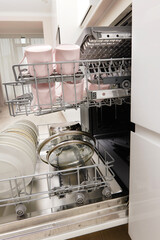 Open built-in dishwasher machine with clean cutlery, dishes, plates in white modern kitchen