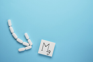 Medical pills in arrow shape with icon of  magnesium on blue background. Nutritional supplement concept. Top view, flat lay. Space for text. - obrazy, fototapety, plakaty