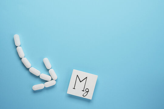 Medical pills in arrow shape with icon of  magnesium on blue background. Nutritional supplement concept. Top view, flat lay. Space for text.