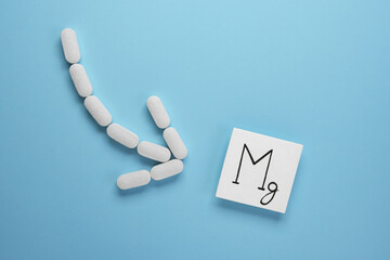 Arrow made of white pills on a blue background. Pills of Magnesium on blue background. Concept of vitamin Mg. Top view, flat lay.