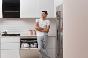 handsome husband man using dishwasher and washing dishes in white modern kitchen. copy space