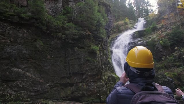 A beautiful waterfall in a mountainous area. A tourist takes pictures of nature on a smartphone. Slow motion
