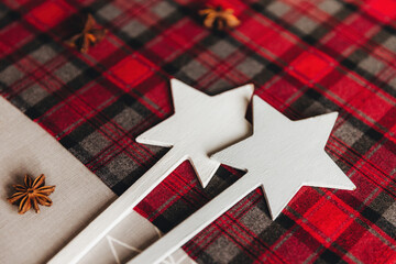 Close-up of white wooden stars on festive red and black plaid fabric, accented with anise stars