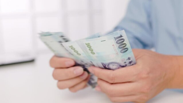 close-up of male hands counting a stack of hundred-dollar Taiwan banknotes.New Taiwan Dollar