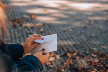 Woman opens a white envelope while sitting on a park bench. 