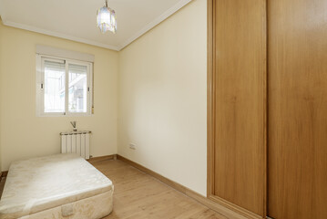 A room in an apartment with a built-in wardrobe with sliding oak doors with a small couch without a mattress and cream-colored walls