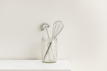 A clear glass jar with metal kitchen utensils on a white wooden cabinet
