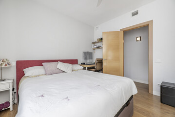 A double bedroom in an apartment with a headboard upholstered in red fabric, a small desk behind the door and a wooden floor