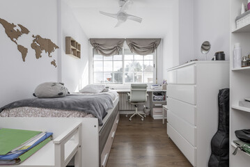 A youth bedroom with a desk under the French-style aluminum window, white furniture and matching...