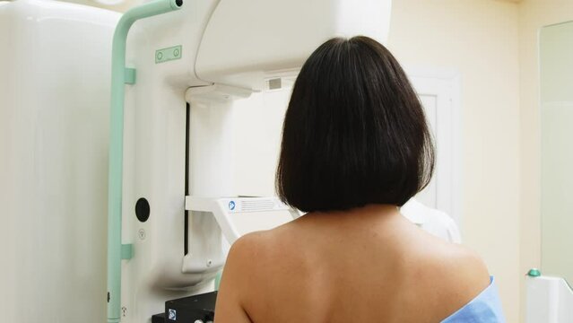 Hospital radiology room. A young woman stands during a mammography procedure. A female doctor adjusts a digital mammography machine for a patient. Prevention of breast cancer. Modern clinic.