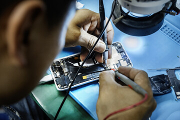 A technician repairing a mobile phone at his work table - obrazy, fototapety, plakaty