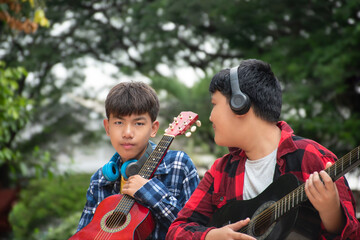 Asian boys are playing acoustic guitar at school park before going to join school summer camp.