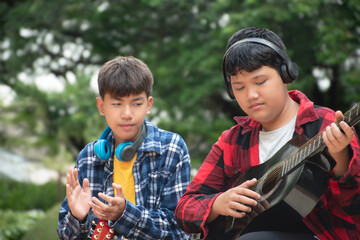 Asian boys are playing acoustic guitar at school park before going to join school summer camp.