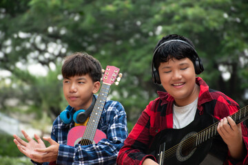 Asian boys are playing acoustic guitar at school park before going to join school summer camp.