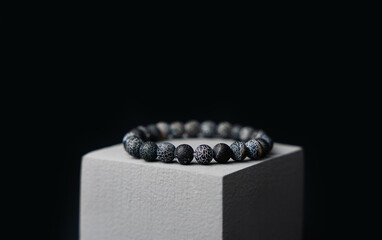 Natural stone bracelet on a gray podium on a black background. Close-up.