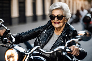 Naklejka premium Happy beautiful elderly senior woman with grey hair rides a motorcycle along a city street, laughing and smiling, mature old biker in black leather jacket