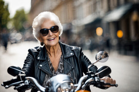 Happy beautiful elderly senior woman with grey hair rides a motorcycle along a city street, laughing and smiling, mature old biker in black leather jacket