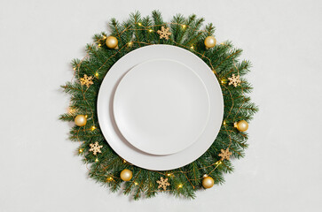 Empty plate in a Christmas wreath with golden festive decorations on a white background. New Year table setting. Preparing for Christmas dinner. Top view, flat lay.