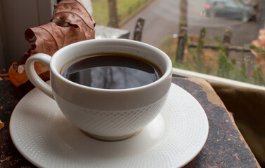 A white porcelain cup with strong black coffee on a saucer stands on a stack of old books against...