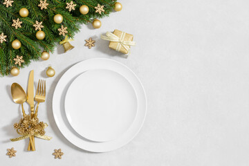 Christmas table setting with empty white plate and gold decor on a white background. New Year serving. Template for menu or design. Festive dinner. Copy space, top view, flat lay.