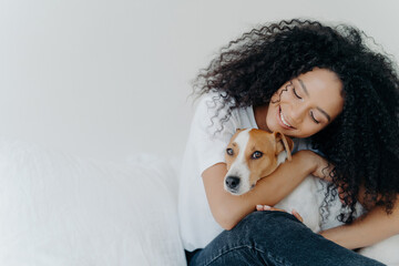 Serene woman with curly hair lovingly embracing her dog, sharing a peaceful moment