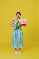 Smiling. Portrait of stylish woman emotionally posing with present boxes over yellow background