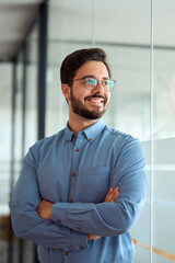 Happy young latin business man leader looking aside standing arms crossed in office hallway....