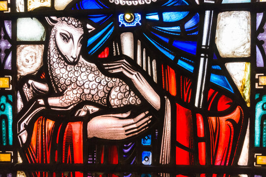 Stained glass window in a church showing Jesus holding a lamb and depicted as a shepherd