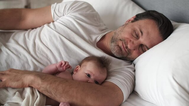 The father wakes up with the baby in the morning lying on the bed.