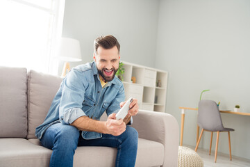 Photo of cheerful carefree man arms hold phone playing games open mouth smile free time home indoors