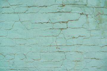 A mint green old wall with a cracked and peeling paint texture. 