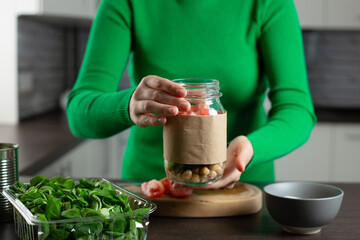 Woman making vegan salad in jar with chickpea. Cooking healthy food.