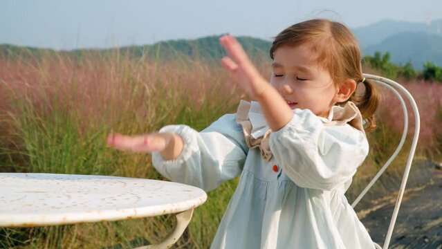 Playful Little Girl Toddler Claping on Table  During Picnic by Pink Muhly Grass or Muhlenbergia Capillaris