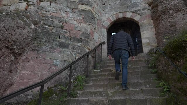 A man walking up stone steps to an archway in an ancient brick building, castle or fortress