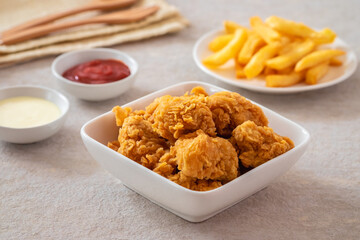 Crispy popcorn chicken in bowl with french fries on plate and sauce.
