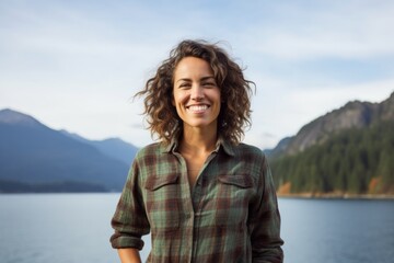 Fototapeta premium Portrait of a happy woman in her 40s wearing a comfy flannel shirt against a panoramic mountain vista. AI Generation