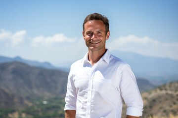 Fototapeta na wymiar Portrait of a smiling man in his 40s wearing a classic white shirt against a panoramic mountain vista. AI Generation