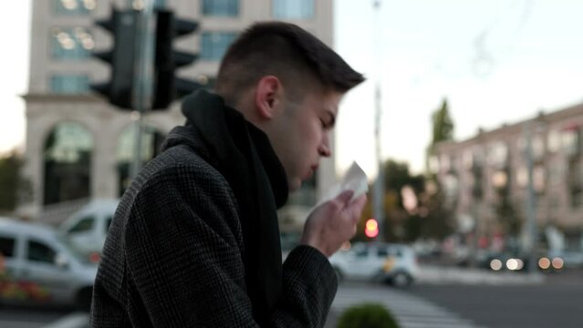 City Strain A young man endures persistent sneezing and coughing, visibly affected by the flu symptoms while outdoors.