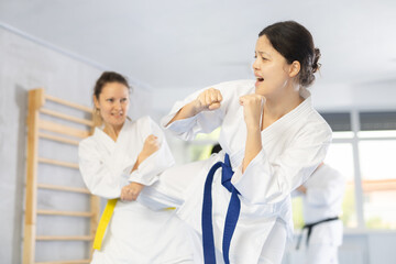 Fototapeta premium Adult woman and young woman in kimono train judo techniques in group in studio