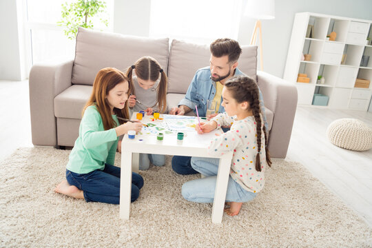 Full body portrait of four persons man spend free time with cute positive girls painting sit on carpet behind desk indoors