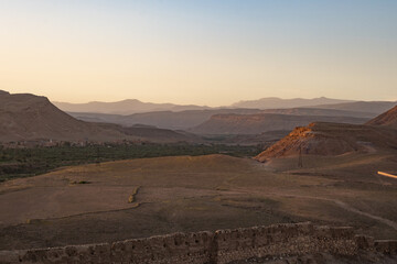 Orange stone desert hills seen in the Morocco Atlas mountains with a mud wall in front