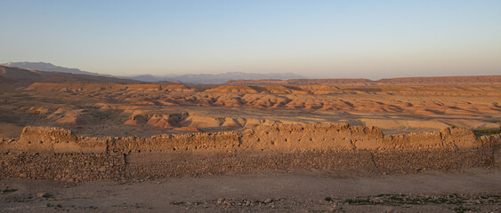 Orange stone desert hills seen in the Morocco Atlas mountains with a mud wall in front