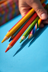 Colorful pencils and crayons holding in hand on a blue background 
