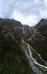 Aerial panorama of a Shdugra waterfall. Vertical photo. The high Caucasian mountains, Mount Ushba in the background. Stormy flow of mountain Dolra river. Vacation and travel, hiking in Mazeri, Georgia
