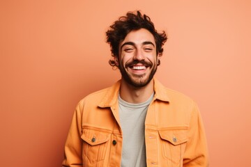 Fototapeta premium Portrait of a happy man in his 20s sporting a rugged denim jacket against a pastel orange background. AI Generation